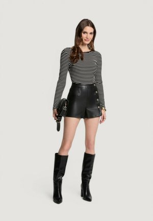 Mini pantaloni in pelle nera con bottoni laterali, abbinati a un top a righe bianche e nere a maniche lunghe. Stivali neri alti fino al ginocchio completano il look.