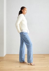 Fehér bolyhos pulóver egy fehér peplum toppon, világoskék bőrnadrággal és beige pántos magassarkúval párosítva. Simító felület, laza dizájn.