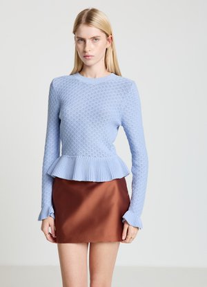 Pull en maille bleu clair avec un ourlet à basque, présentant un motif texturé et des poignets à volants, associé à une jupe en satin marron.