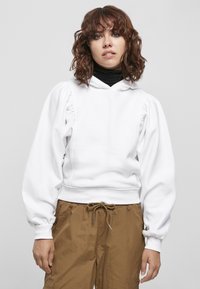 Felpa bianca con maniche a sbuffo, orlo a coste e cappuccio con coulisse. Abbinata a pantaloni marroni chiari con vita elasticizzata e coulisse.