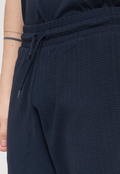 Pantaloni jogger in blu navy con una texture a coste, vita elasticizzata e cordino regolabile. Presentano tasche laterali per una maggiore funzionalità.