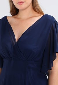 Vestido azul marino de cuello en V, confeccionado en tela ligera, con mangas cortas fluidas y cintura fruncida para una silueta favorecedora.