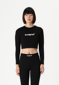 Black long-sleeve crop top and high-waisted leggings, both featuring a white "lowlights" logo. Sleek, form-fitting design, smooth texture.