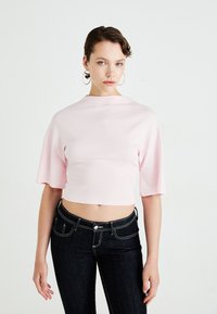 Lyserosa crop-top med brede ermer, laget av glatt stoff. Kombinert med mørke jeans med kontraststing.