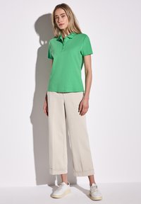 Grön kortärmad pikétröja i bomull, med flat krage, kombinerad med krämfärgade vida byxor, bärs tillsammans med vita sneakers.