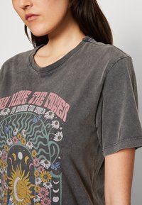Šedé grafické tričko s krátkými rukávy, kulatým výstřihem. Obsahuje barevný květinový a sluneční design s textem, měkká textura, vintage vzhled.