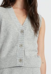 Cardigan senza maniche grigio realizzato in morbido tessuto a maglia, con scollo a V, orlo a coste e tre bottoni sulla parte anteriore.
