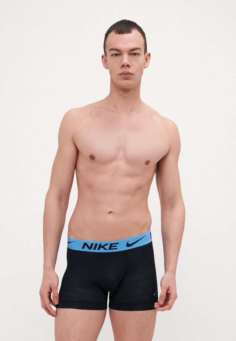 Sorte Nike boxershorts med en lys blå midjebånd som har merkevarenavnet. Glatt tekstur og tettsittende design. Modellen er vendt mot kameraet.