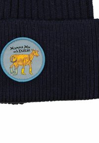 Marinblå ribbad mössa med en cirkulär ljusblå lapp som har en illustration av en gul ko i gröna stövlar. Texten säger "Mamma Mu och Kråkan."