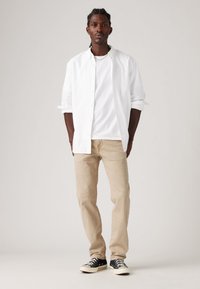 Witte overhemd met knopen over een wit T-shirt, gecombineerd met beige broek en zwarte sneaker. Glad materiaal en een relaxte pasvorm overal.