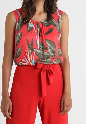 Red top with leaf pattern, round neckline, sleeveless design. Paired with high-waisted red trousers featuring a tied bow accent.