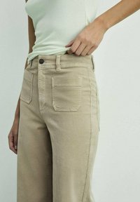 Beige corduroy pants with a straight leg, featuring two front pockets, a single metal button closure, and vertical ribbed texture.
