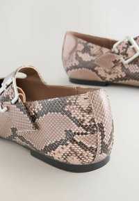 Pink snakeskin flats with black accents, featuring a geometric buckle and a smooth texture. The design includes a low heel for comfort.