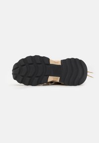 Semelle extérieure en caoutchouc noir avec une surface texturée et un motif de rainure défini. La semelle intermédiaire beige offre un contraste et un soutien.