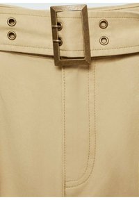 Beige stoffen riem met een rechthoekige metalen gesp. Kenmerkt zich door metalen oogjes en stiksels, wat zorgt voor een zachte textuur en een verfijnd ontwerp.
