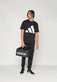 Juoda marškinėliai su balta trijų juostų logotipu, juodos kelnės ir juodas sportinis maišas su baltu „adidas“ tekstu. Batai su trijų juostų akcentais.