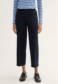 Marineblauwe broek met een rechte snit en cropped lengte, gemaakt van een gladde stof. Gecombineerd met zwarte veterschoenen en een blauw gestreept top.