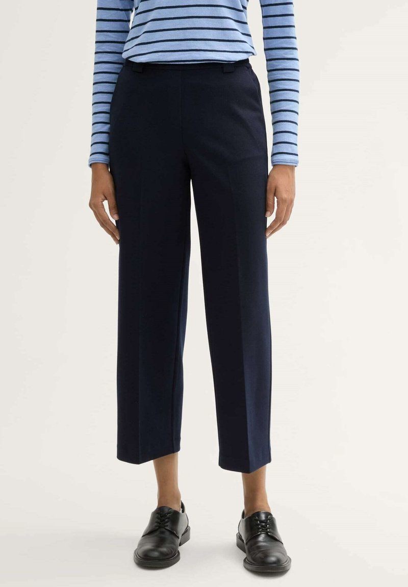 Marineblauwe broek met een rechte snit en cropped lengte, gemaakt van een gladde stof. Gecombineerd met zwarte veterschoenen en een blauw gestreept top.