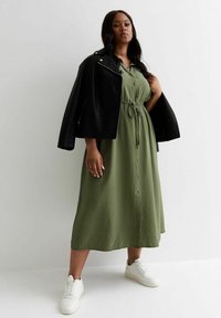 Olivgrön skjortklänning med knyt-hand midja, tillsammans med en svart läderjacka och vita sneakers, med en avslappnad passform och mjuk textur.