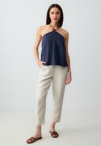 Top halter in lino navy con silhouette dritta, abbinato a pantaloni in lino beige chiaro e sandali piatti marroni con cinturini intrecciati.