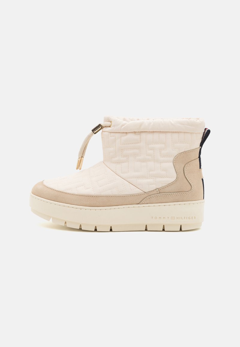 Beige polstret ankelstøvle med snøring og guldfarvet hardware. Har en suede tåhætte og struktureret logo-detaljering på siden. Tykk sål.