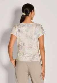 Korte mouwen top in een lichte bloemenprint met zachte pastelkleuren. Glad materiaal met een ontspannen pasvorm, ronde halslijn en subtiele textuurdetails.