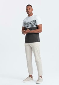 Tričko s krátkým rukávem s bílým a šedým designem palmového listu na horní části, kombinované s světle béžovými slim-fit kalhotami a béžovými teniskami.