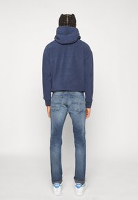 Marineblauwe hoodie met een hoge kraag en manchet, gecombineerd met lichtblauwe jeans. Witte sneakers met blauwe accenten maken de look compleet.