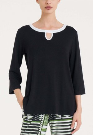 Donna con indosso una maglia nera a maniche lunghe con bordi bianchi e scollo a goccia, abbinata a pantaloni con motivo geometrico verde, bianco e nero.