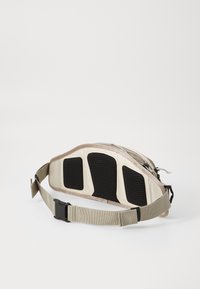 Marsupio con design curvo; realizzato in tessuto beige, presenta accenti in rete nera, una chiusura con zip e una tracolla regolabile.
