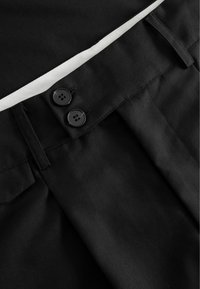 Melni bikses ar gludu audumu, izplešu dizainu, divām melnām pogām un baltu akcenta joslu pie jostas.