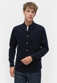 Mörkblå kord skjorta med långa ärmar, knappad krage och vita knappar. Har en slät yta och rak fåll.