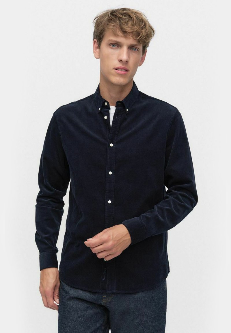 Mörkblå kord skjorta med långa ärmar, knappad krage och vita knappar. Har en slät yta och rak fåll.