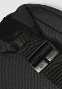 Bolso mensajero negro con superficie de tela texturizada, que cuenta con una hebilla y una correa negras mate para un cierre seguro. Diseño duradero y práctico.