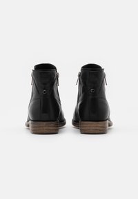 Botas de tobillo de cuero negro con textura suave, cierre de cremallera y tacón de madera marrón. Presenta costuras mínimas y un diseño elegante.