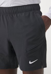 Shorts deportivos negros con cintura elástica, bolsillos laterales, logo de Nike en blanco y una textura suave; diseñados para la comodidad y la flexibilidad.
