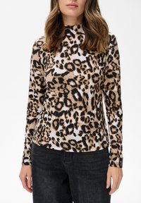 Długi rękaw bluzki z wzorem w panterkę w brązowo-czarnych odcieniach na jasnym tle, z wysokim dekoltem i dopasowanym krojem.