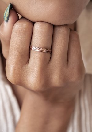 Roze gouden gevlochten ring gedragen op een vinger, met een gestructureerd oppervlak en een gladde binnenband, tegen een neutrale huidtint.