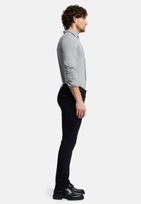 Grå langærmet skjorte, sorte slim-fit jeans og sorte snørebåndssko. Sidesyn viser skjortens stof og skræddersyede pasform.