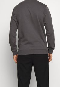 Gray sweatshirt with a crew neckline, ribbed cuffs, and hem, made from soft fabric. Worn with black pants, displayed from the back.