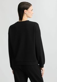Zwarte, lange mouwen sweatshirt met een relaxte pasvorm, geribbelde manchetten en een ronde hals. Zachte stof en minimalistisch ontwerp, geschikt voor casual wear.