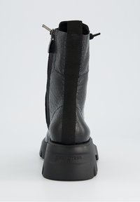 Botín negro con cuero sintético texturizado, paneles laterales elásticos y suela de goma gruesa. Presenta un detalle de cremallera metálica.
