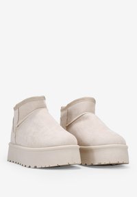 Botas de tobillo beige de ante, con punta redonda, corte bajo y una suela de plataforma gruesa y texturizada con bordes estriados.