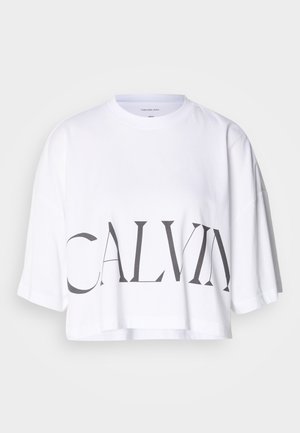 Witte cropped t-shirt van katoen, met in het groot zwarte letters "CALVIN" op de voorkant. Korte mouwen en een relaxed fit.