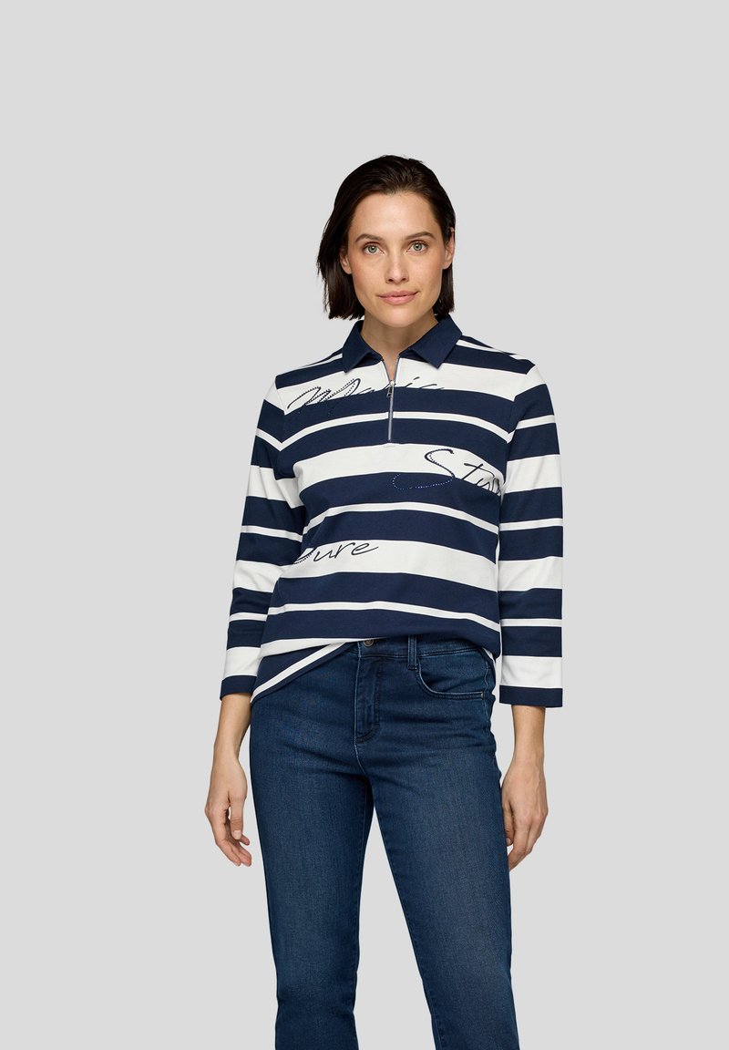 Marineblau-weiß gestreiftes Langarm-Polohemd mit Reißverschlusskragen, featuring Textelementen und einem lässigen Schnitt, kombiniert mit dunkelblauen Jeans.