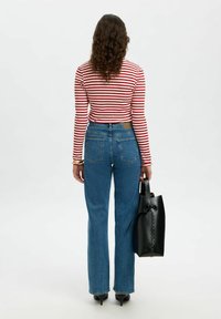 Randig röd och vit långärmad topp i kombination med högmidjade blå jeans, hållande en svart tote-väska med textur.