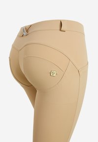 Leggings nudi realizzati in un tessuto morbido e elasticizzato. Presentano una vita bassa e cuciture curve. Piccolo logo decorativo sulla tasca posteriore.