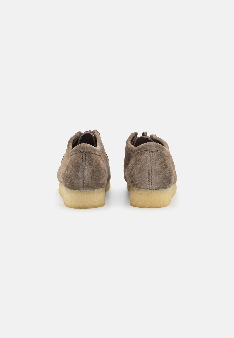 Braune Wildlederschuhe mit einer niedrigen, beigen Gummisohle und einer runden Zehenpartie. Die Rückseite weist Nähte und eine Lasche am Absatz auf.