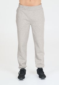 Hellgraue Jogginghosen aus weichem Stoff, mit einem elastischen Bund und schmal zulaufenden Beinen. Kombiniert mit schwarzen Sportschuhen.