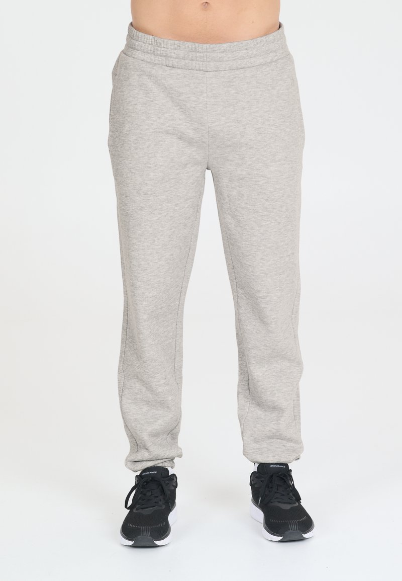 Hellgraue Jogginghosen aus weichem Stoff, mit einem elastischen Bund und schmal zulaufenden Beinen. Kombiniert mit schwarzen Sportschuhen.